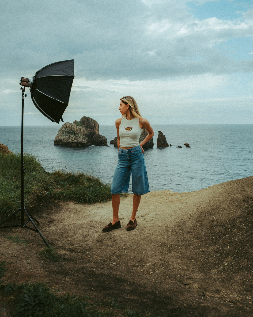 Behind the scenes of a Coral Raw photoshoot on a cliff overlooking the ocean, featuring the sustainable Parrot Fish Tank top.